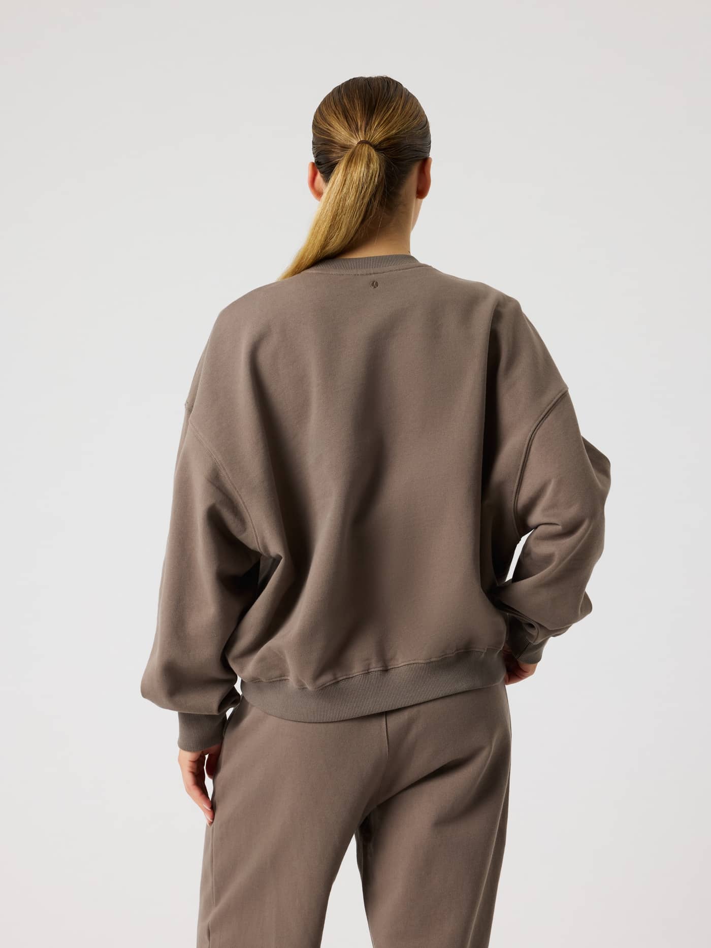 Back view of a model wearing the Studio Oversized Sweatshirt in Falcon (Brown), showcasing the relaxed, oversized fit. - Image 3
