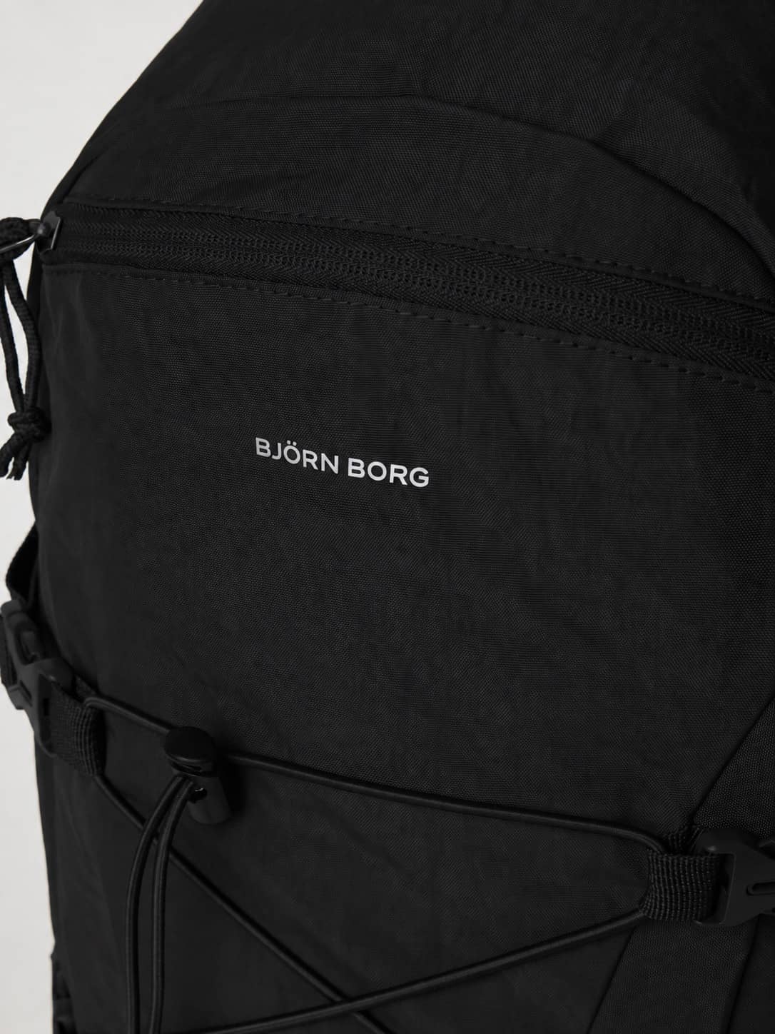Close-up of the Borg Explorer Backpack 28L in Black Beauty (Black) featuring a front zipper pocket and white logo. - Image 4