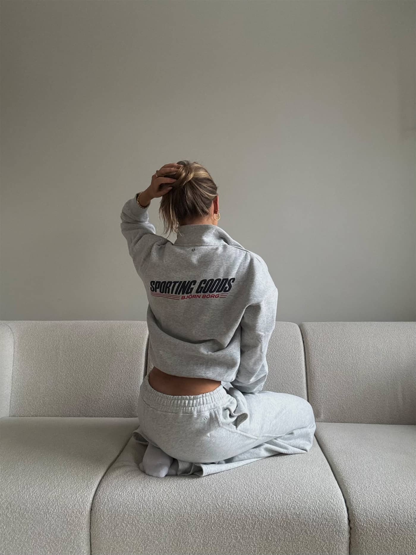 Back view of a woman in the cotton Borg Halfzip Sweatshirt in Ultra Light Grey Melange (Grey) with a black and red logo. - Image 6