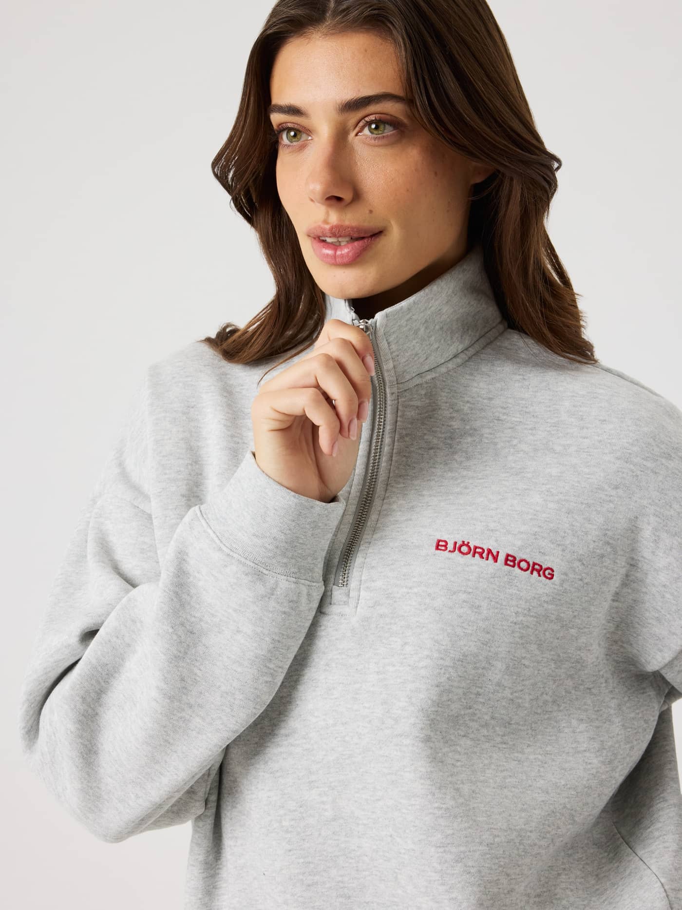 Close-up of a woman wearing the regular fit Borg Halfzip Sweatshirt in Ultra Light Grey Melange (Grey) with a red logo. - Image 7