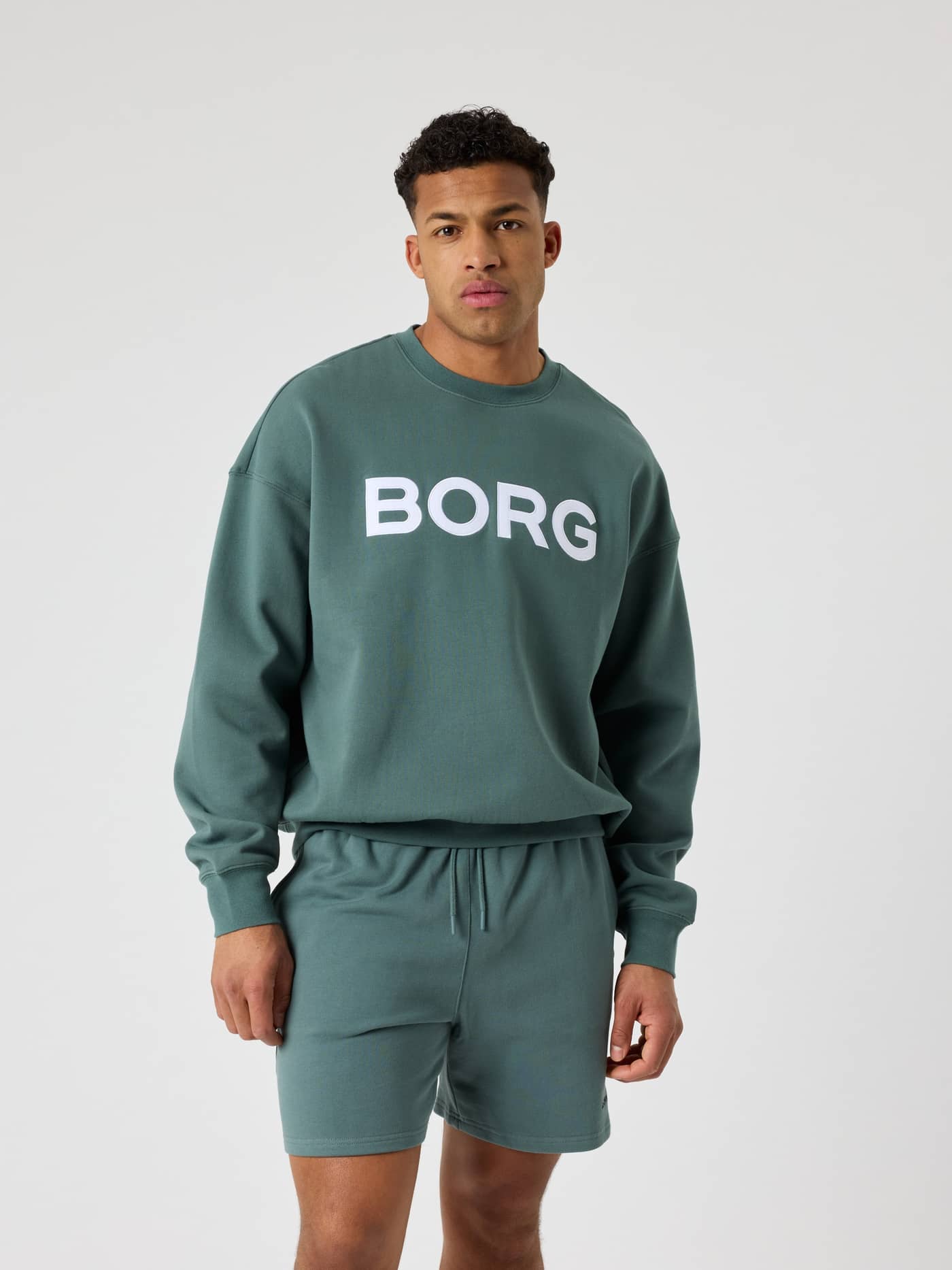 Vorderansicht: Mann im Borg Oversized Logo Sweatshirt in Balsam Green (Grün) aus Baumwolle mit weißem Logo im Tennis-Stil. - Image 2
