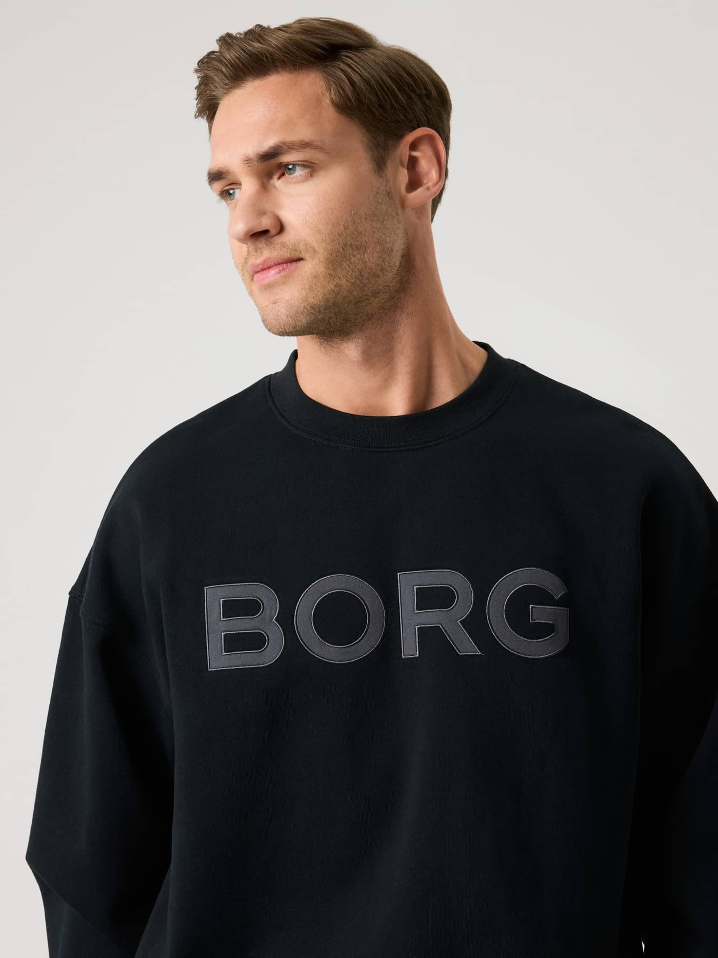 Vorderansicht eines Mannes im Borg Oversized Logo Sweatshirt in Black Beauty (Schwarz) aus weicher Baumwollmischung. - Image 4