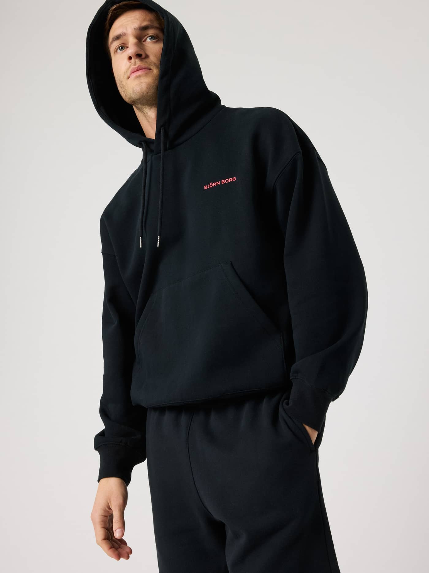 Borg Oversized Hoodie i Black Beauty (Sort) set forfra på en mand med lyserødt logo og funktionel tennis-stil. - Image 4