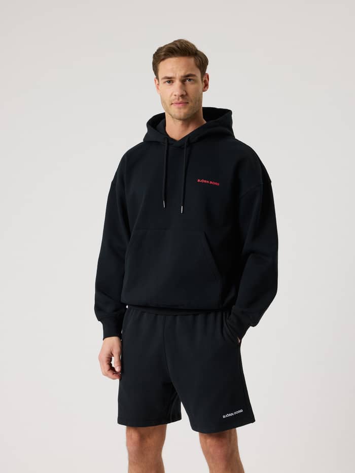 Vorderansicht eines Mannes im Borg Oversized Hoodie in Black Beauty (Schwarz) mit pinkem Logo und Tennis-Details. - Image 2