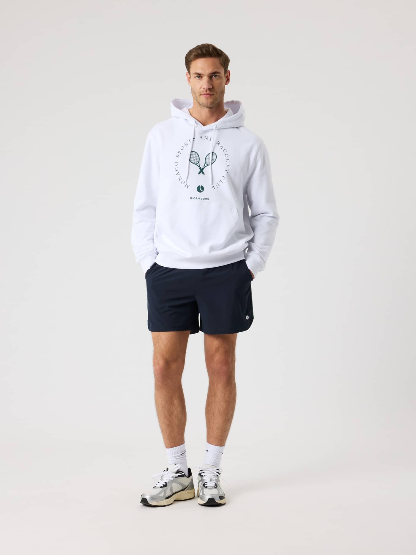 Full-body front view of a man in the Björn Borg Classic Print Hoodie in Brilliant White (White) with a green tennis logo. - Image 5