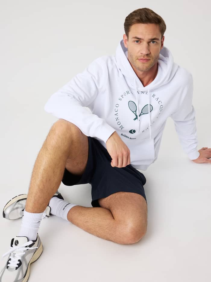 Seated front view of a man wearing the cotton Borg Classic Print Hoodie in Brilliant White (White) with a tennis graphic.