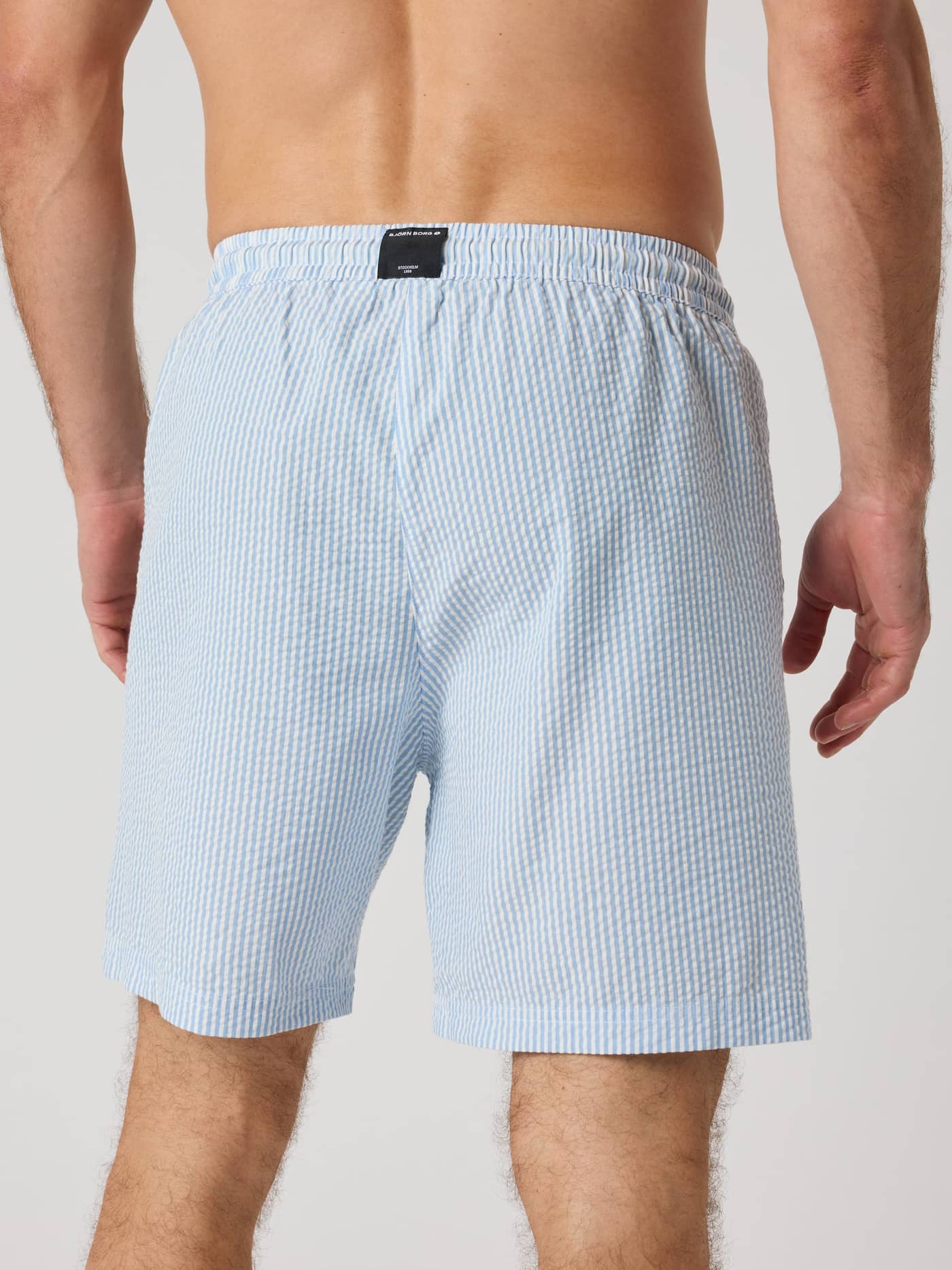 Vista posterior de un hombre con los Borg Seersucker Resort Shorts en Shirt Stripe 1 (Azul) a rayas y etiqueta de logo negra. - Image 2
