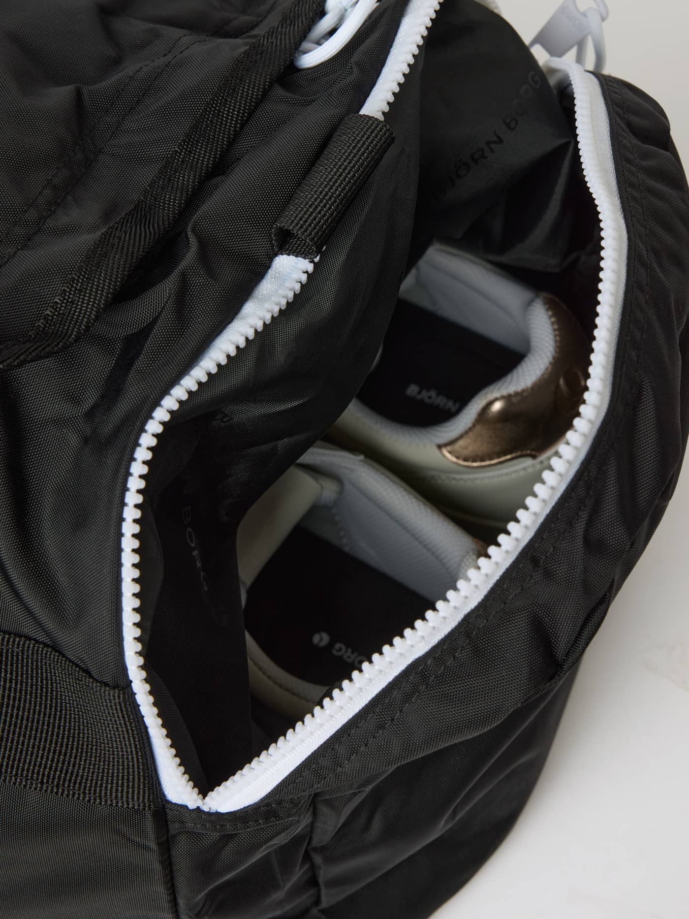 Detailed side pocket of the Black Beauty (Black) Borg Logo Sports Bag 42L, featuring a white zipper and training shoes. - Image 4