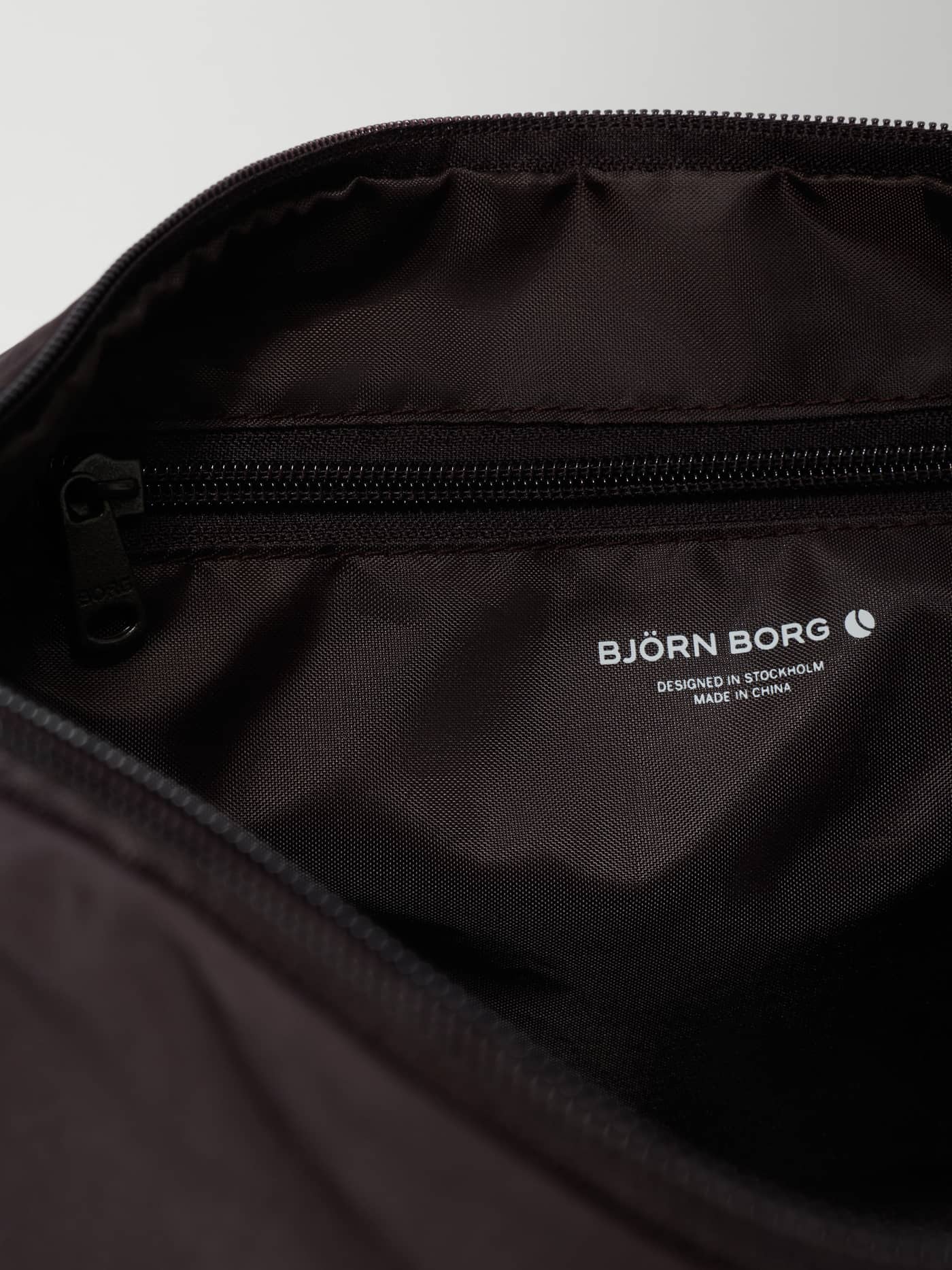 Interior detail of the Studio Active Shoulder Bag 20L in Coffee Bean (Brown) with a white logo and zip pocket for training. - Image 2