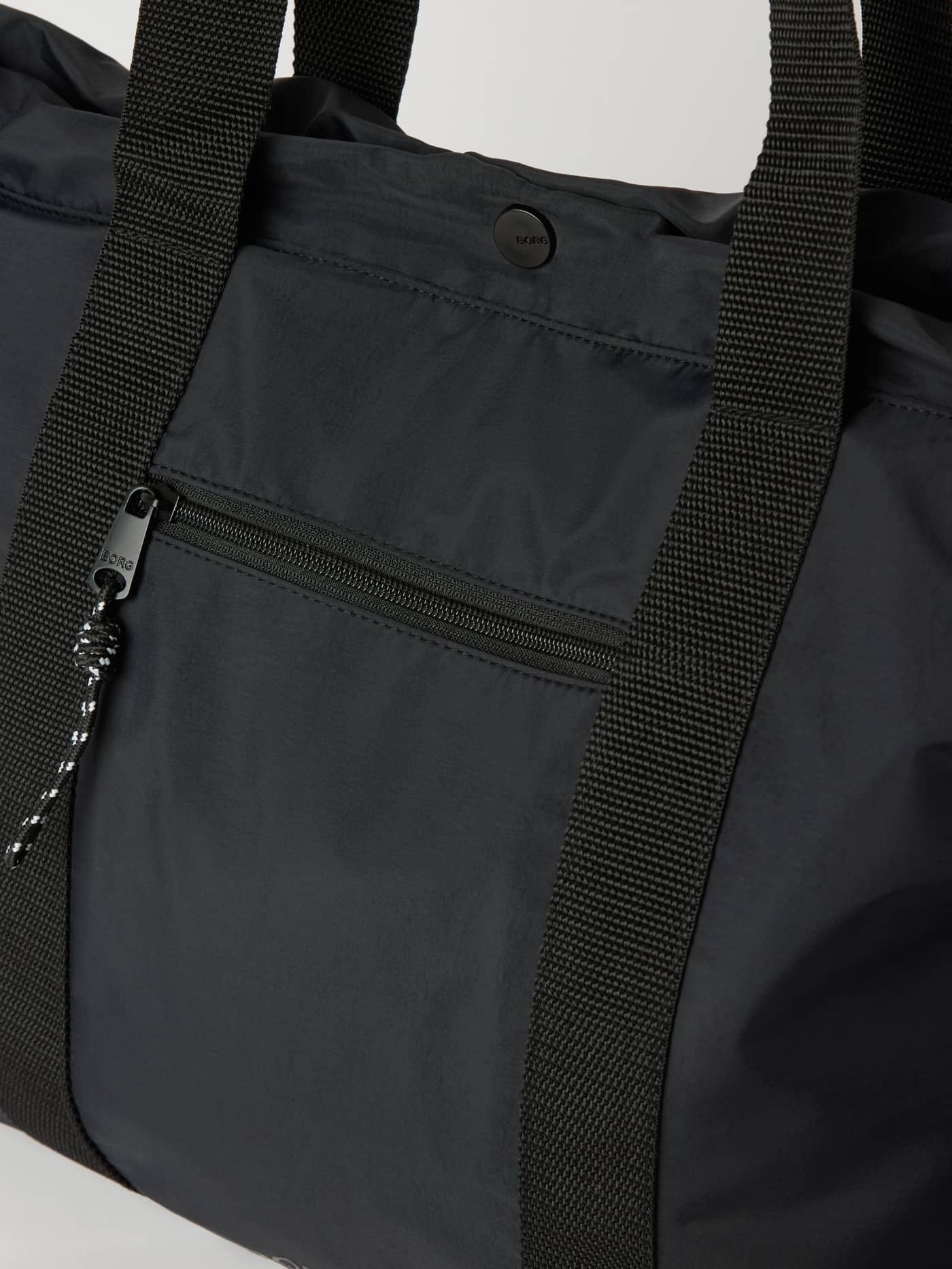Studio Active Tote 18L in Black Beauty (Black) for training, with a front zipper pocket and black logo on the snap button. - Image 2
