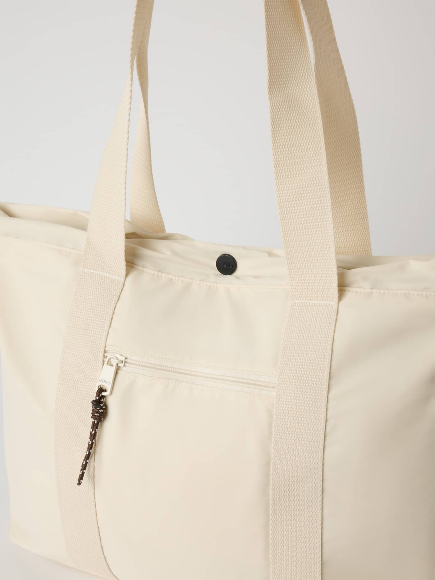 Detailed close-up of the Studio Active Tote 18L in Tofu (White) for training, showing the black BORG snap and front zipper. - Image 3
