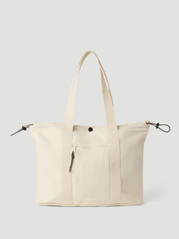Front view of the Studio Active Tote 18L in Tofu (white), a recycled polyester training bag with a front zipper pocket.