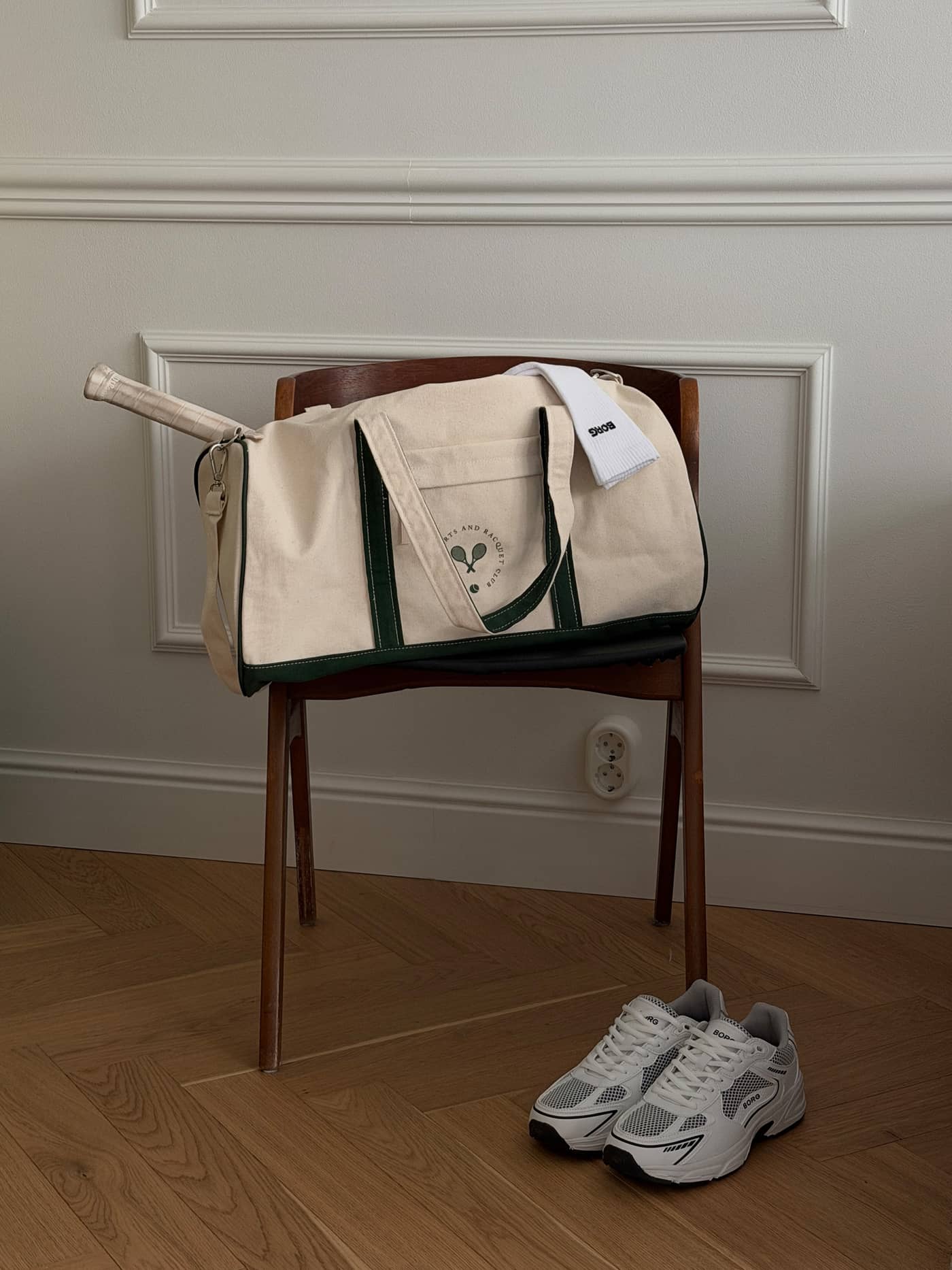 Ace Canvas Sports Bag 40L en Egret (Blanco) de lona de algodón con logo verde para tenis sobre una silla de madera. - Image 1