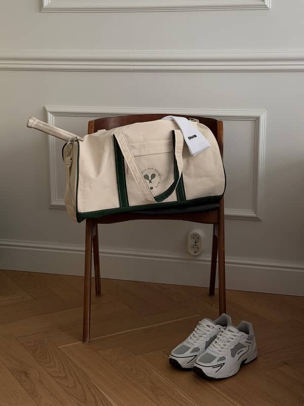 Ace Canvas Sports Bag 40L in Egret (White) made of cotton canvas with a green logo, styled for tennis performance on a chair.
