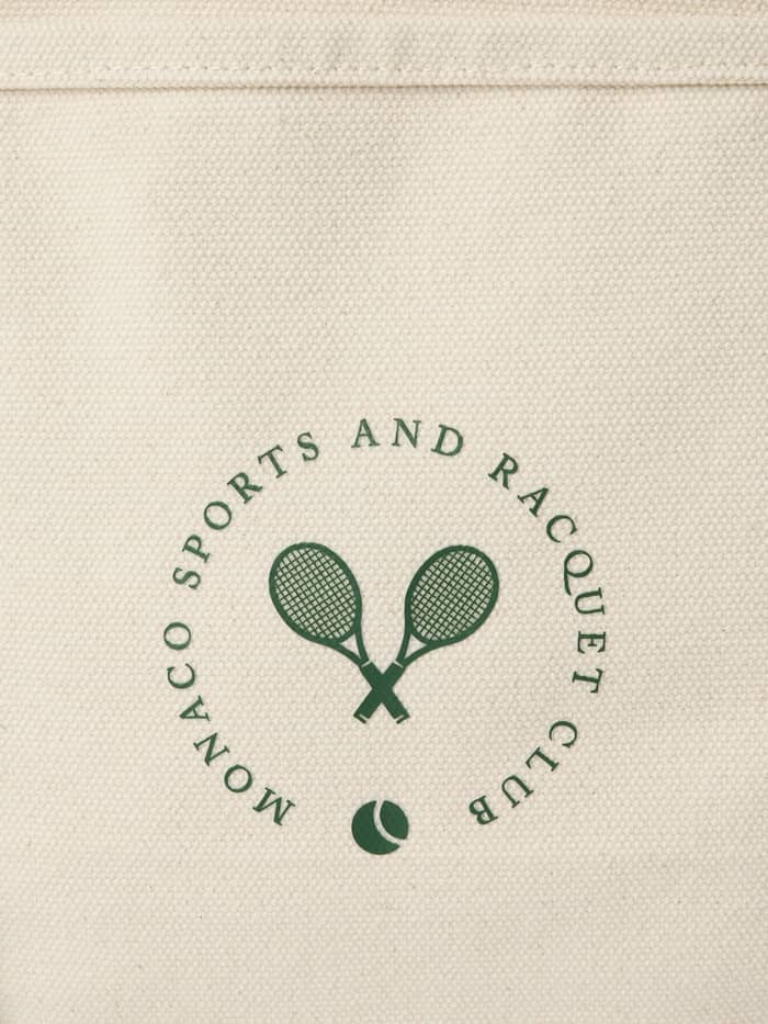 Detailed close-up of the green tennis racquet logo on the cotton Ace Canvas Tote 30L in Egret (White).