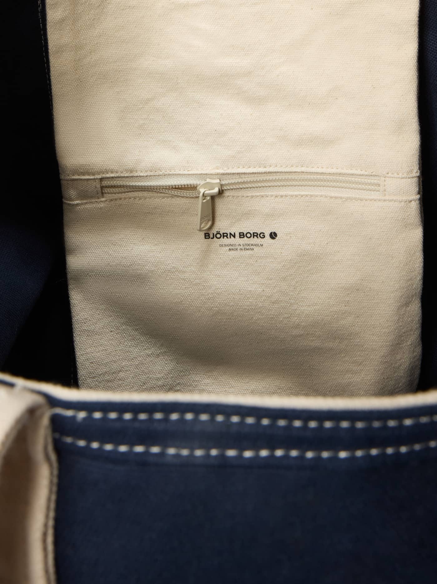 Interior zip pocket and black logo of the Ace Canvas Tote 27L in Night Sky (Navy) for organized tennis court storage. - Image 3