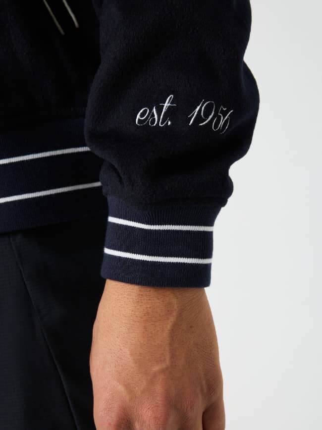 Gros plan de la Borg Varsity Jacket en Night Sky (Marine) avec broderie blanche et poignets rayés inspirés du tennis. - Image 10