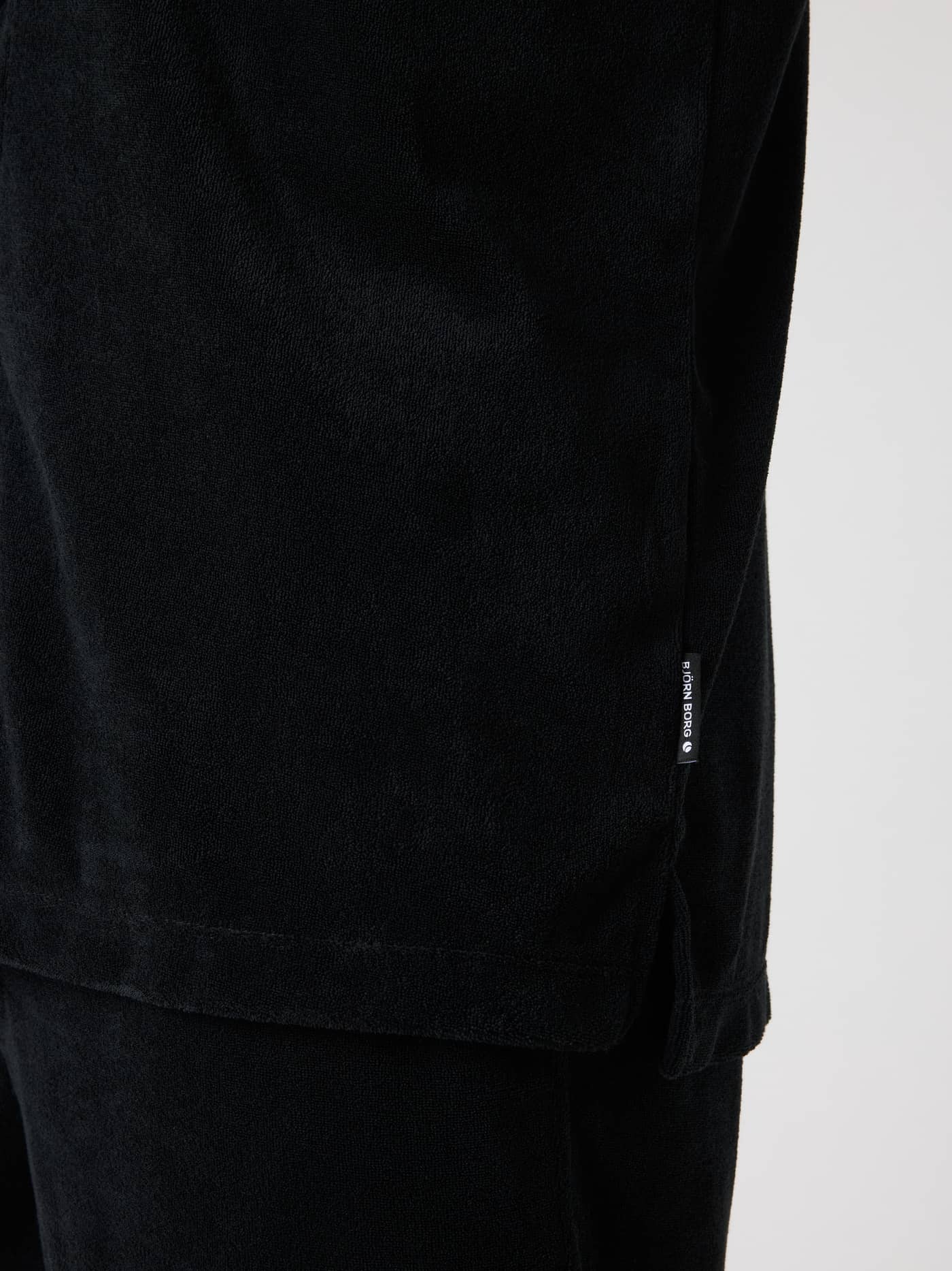 Borg Toweling Pool Shirt i Black Beauty (Sort) i nærbillede med frotté-tekstur, sideslids og hvidt logomærke. - Image 4