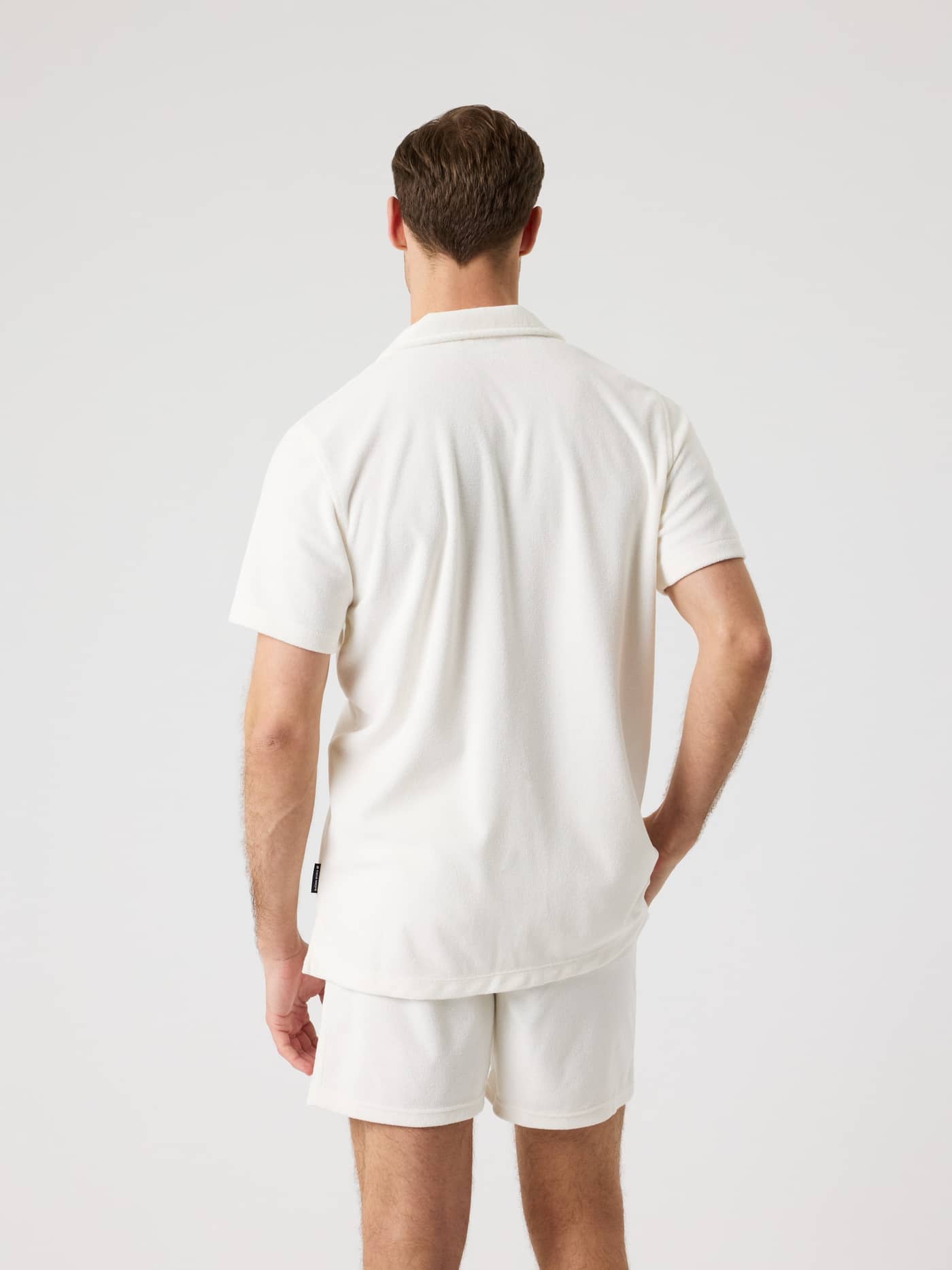 Back view of a man wearing the Tofu (White) Borg Toweling Pool Shirt in soft terry toweling with a black logo label. - Image 2