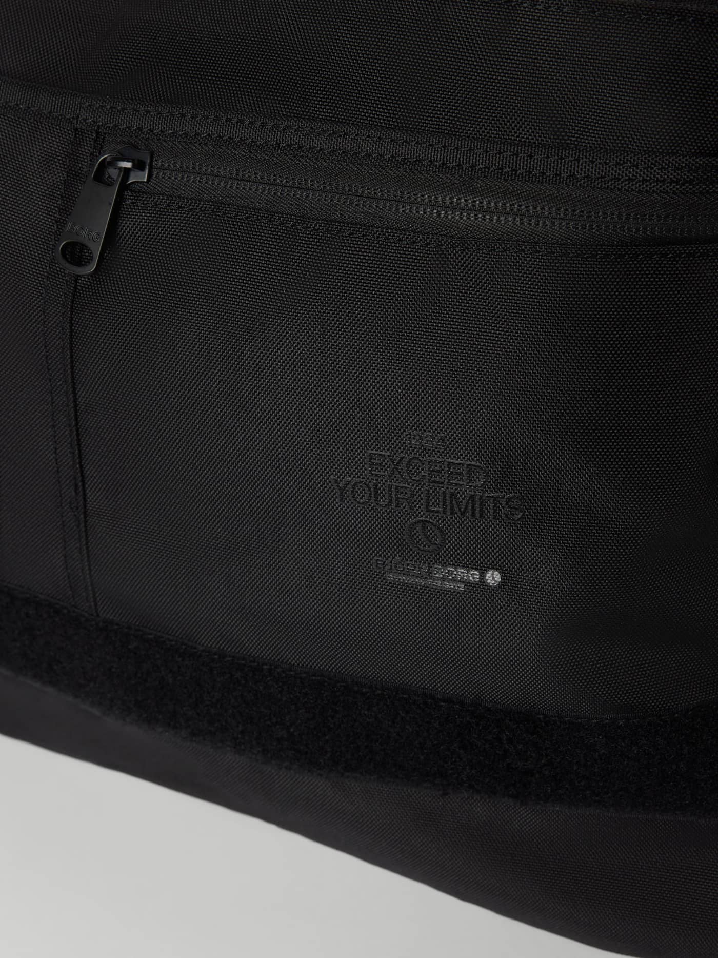 Nahaufnahme der Core Flapbag 12,5L in Black Beauty (Schwarz) mit schwarzem Logo und vorderem Reißverschluss. - Image 3