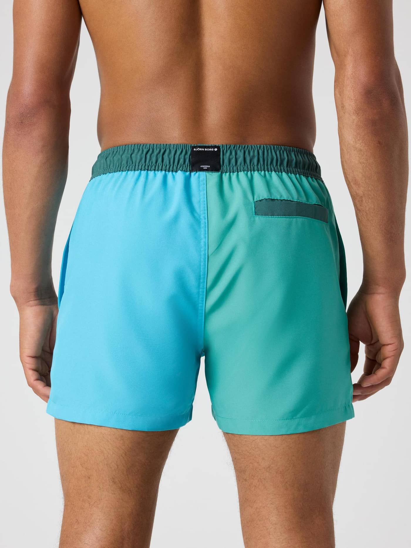 Back view of a man in the regular fit Borg Blocked Swim Shorts in Sea Blue (Blue) made from quick-drying recycled polyester. - Image 2
