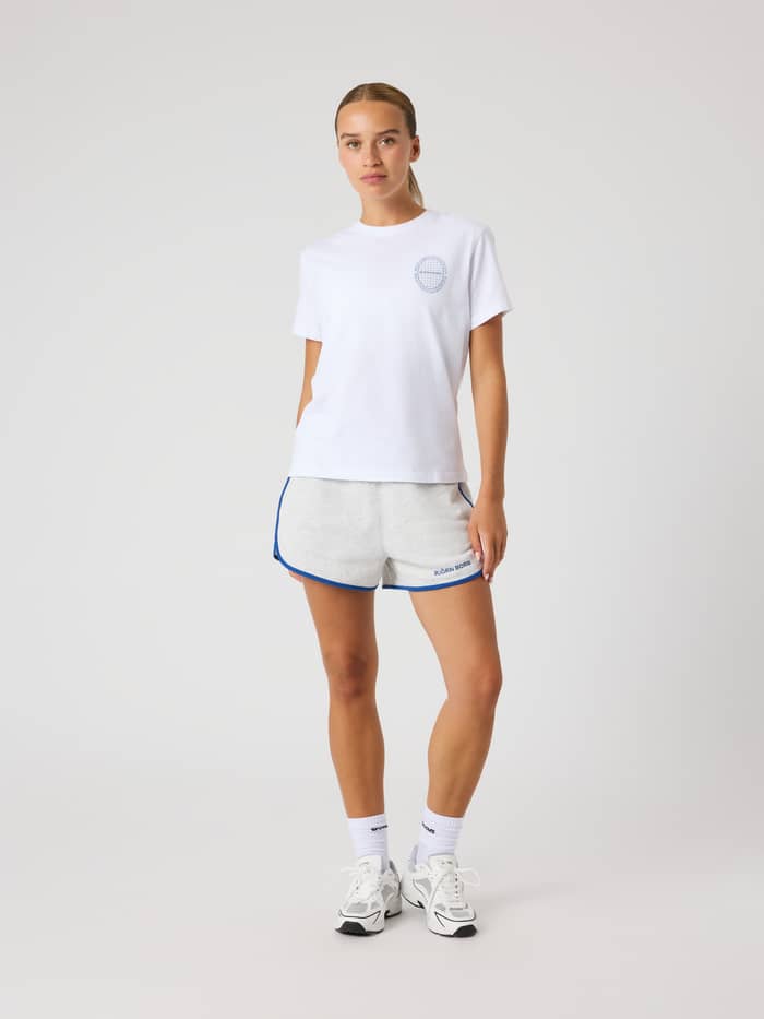 Vorderansicht einer Frau im Borg Cotton T-Shirt in Brilliant White (Weiß) mit blauem Logo und Tennis-Passform.