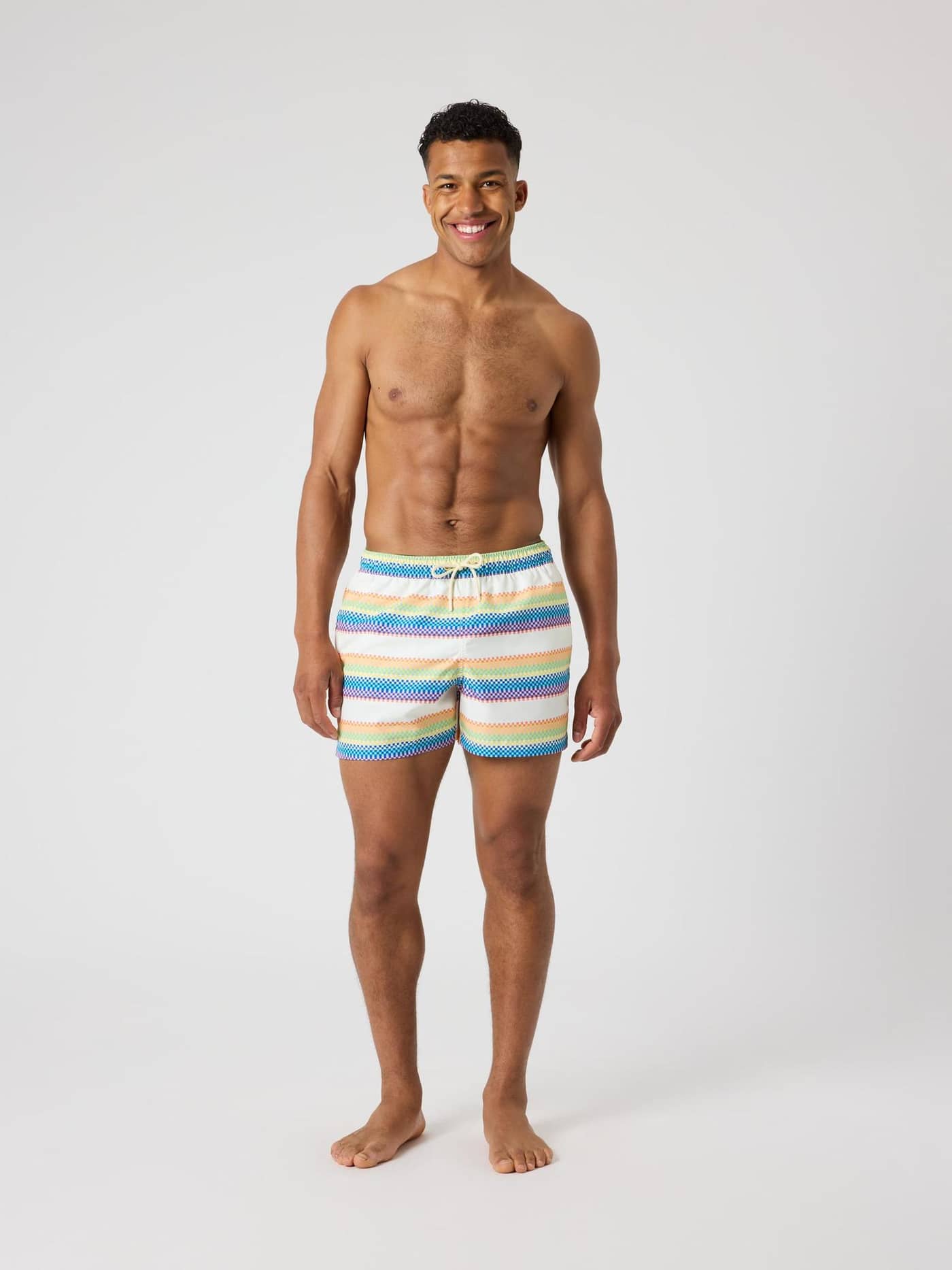 Full-body front view of a man in Björn Borg Print Swim Shorts with blue, orange, and yellow pixel stripes and a regular fit. - Image 3