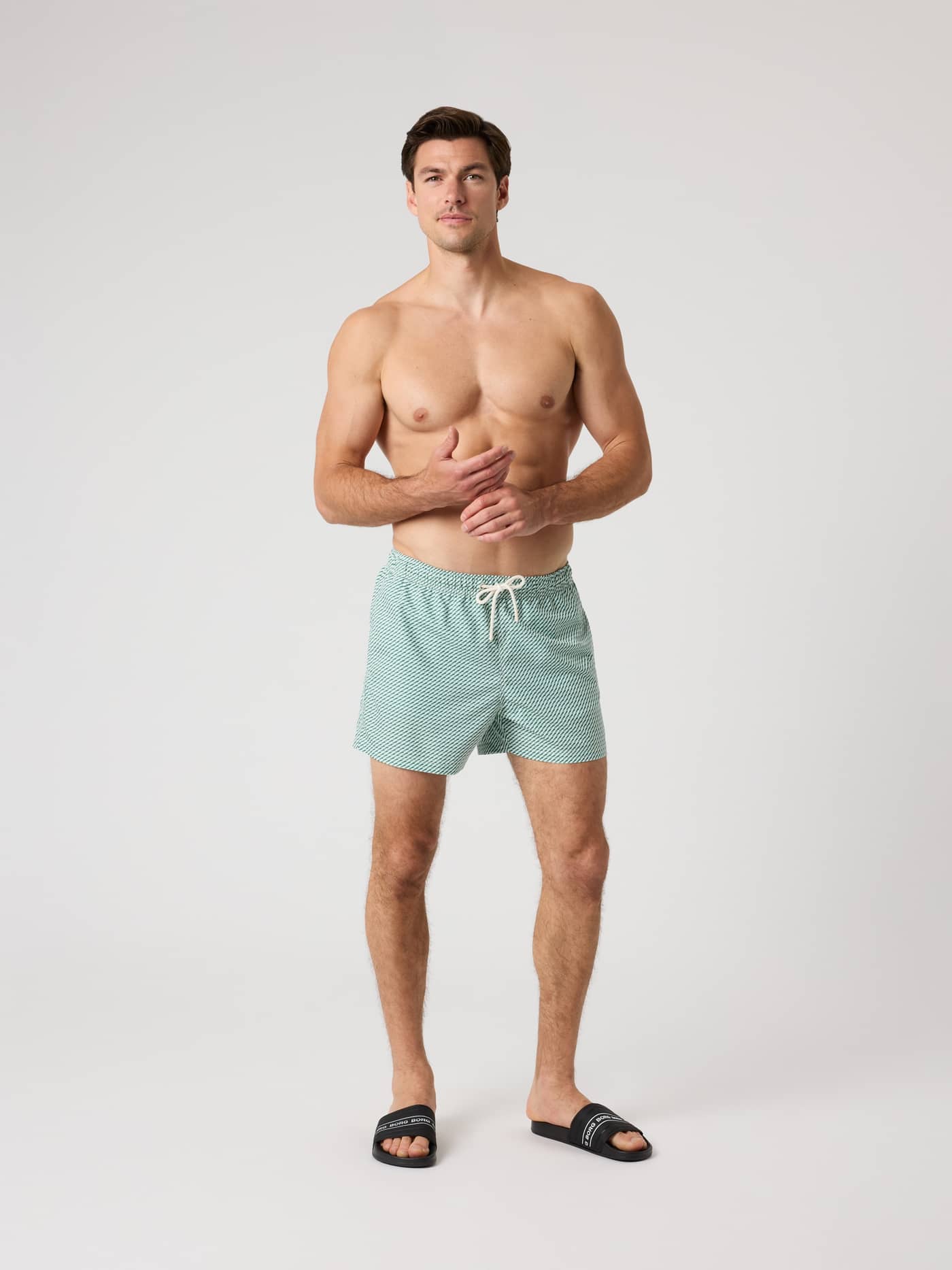 Full-body front view of a man wearing green and white striped Borg Print Swim Shorts with a functional drawstring waist. - Image 3