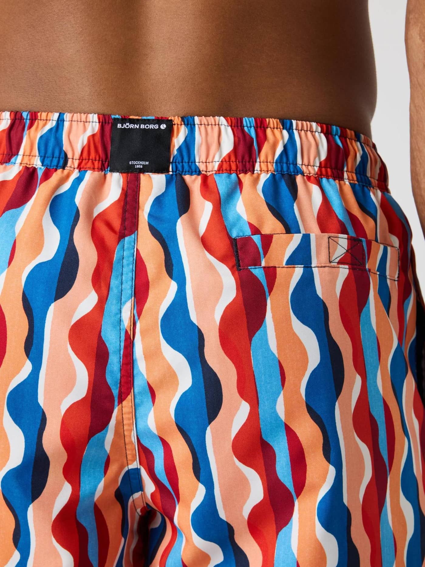 Vista posterior de los Borg Print Swim Shorts con estampado ondulado azul, naranja y rojo y etiqueta de logo negra. - Image 4