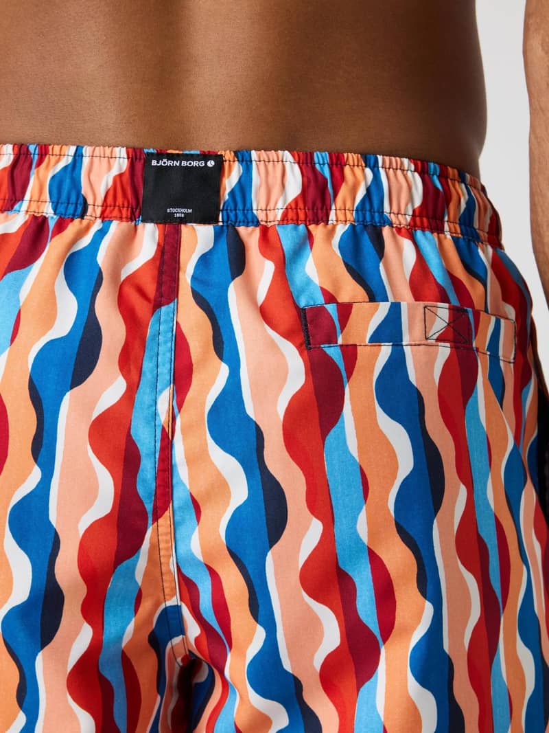 Back view of a man wearing the Borg Print Swim Shorts with a wavy blue, orange, and red print and a black logo label. - Image 4