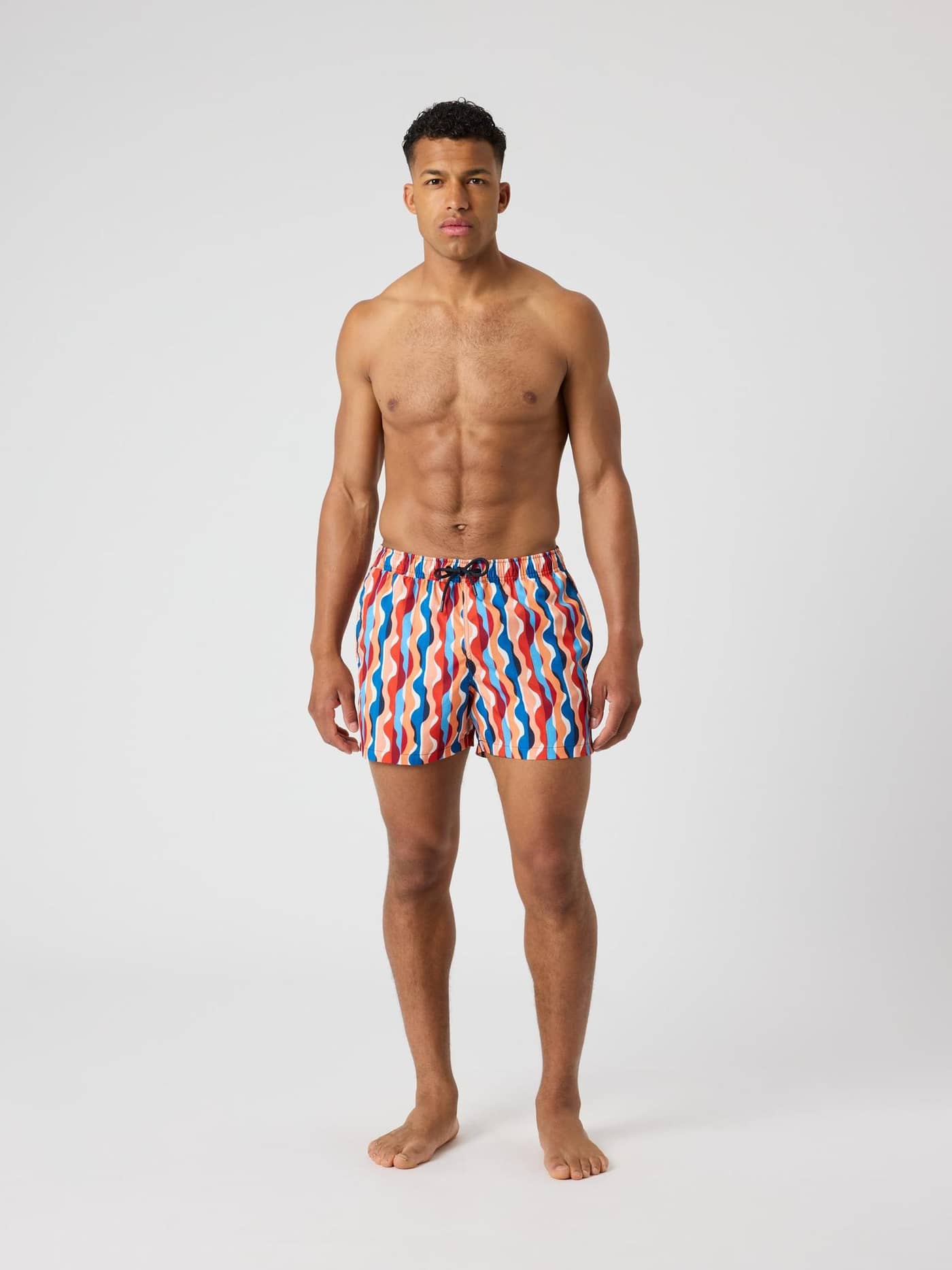 Vista frontal de un hombre con los Borg Print Swim Shorts con estampado digital ondulado en rojo, azul y naranja. - Image 3
