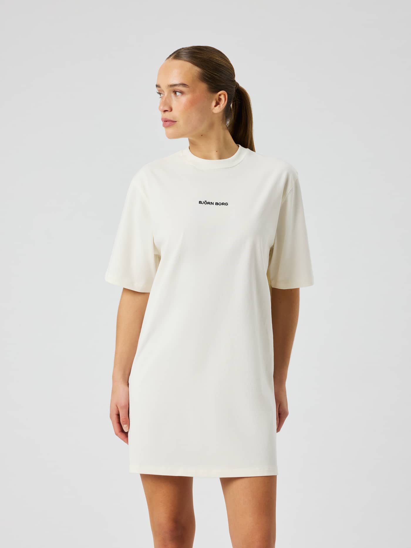 Vue de face d'un mannequin en Studio Oversized T-Shirt Dress en coton Tofu (Blanc) à la coupe ample avec logo noir. - Image 2
