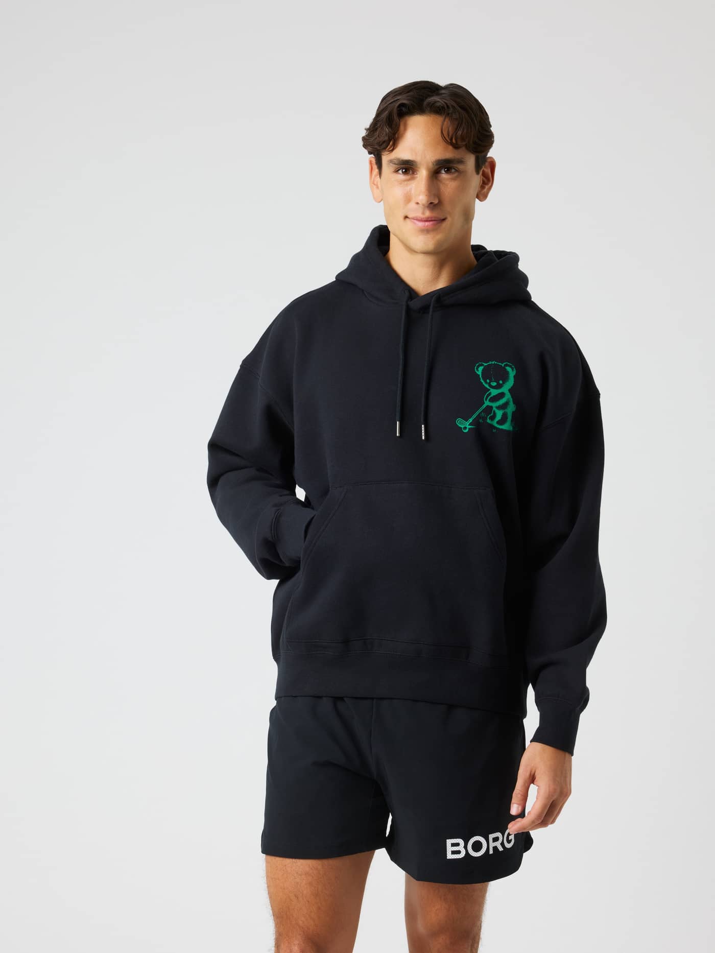 Front view of a man wearing the Borg Oversized Hoodie in Black Beauty (Black) featuring a green bear golf graphic. - Image 1
