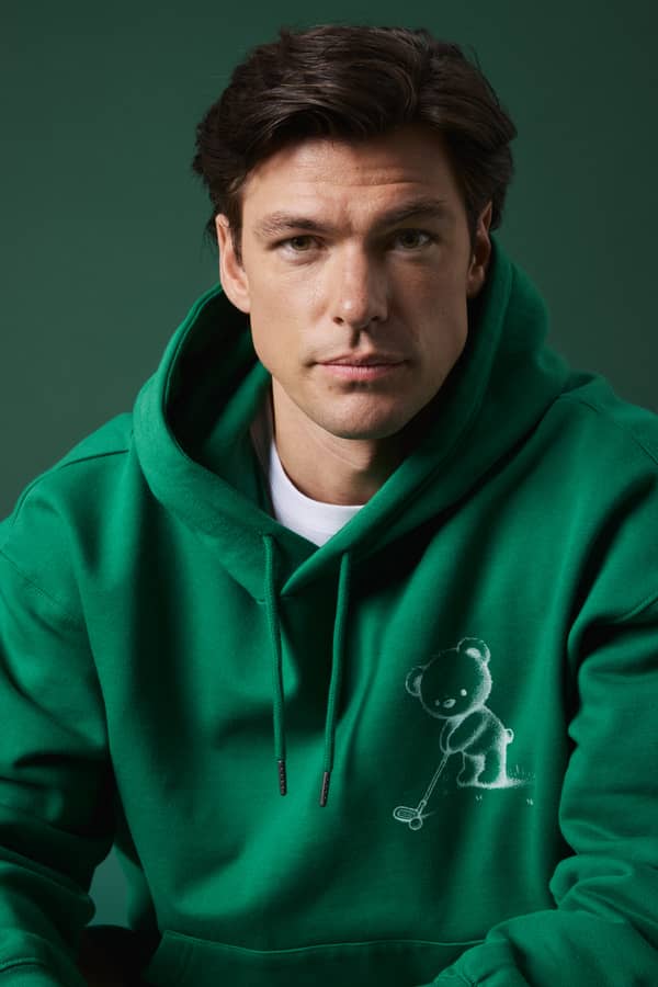 Gros plan d'un homme portant le Borg Oversized Hoodie Verdant Green (Vert) avec un motif d'ours golfeur.