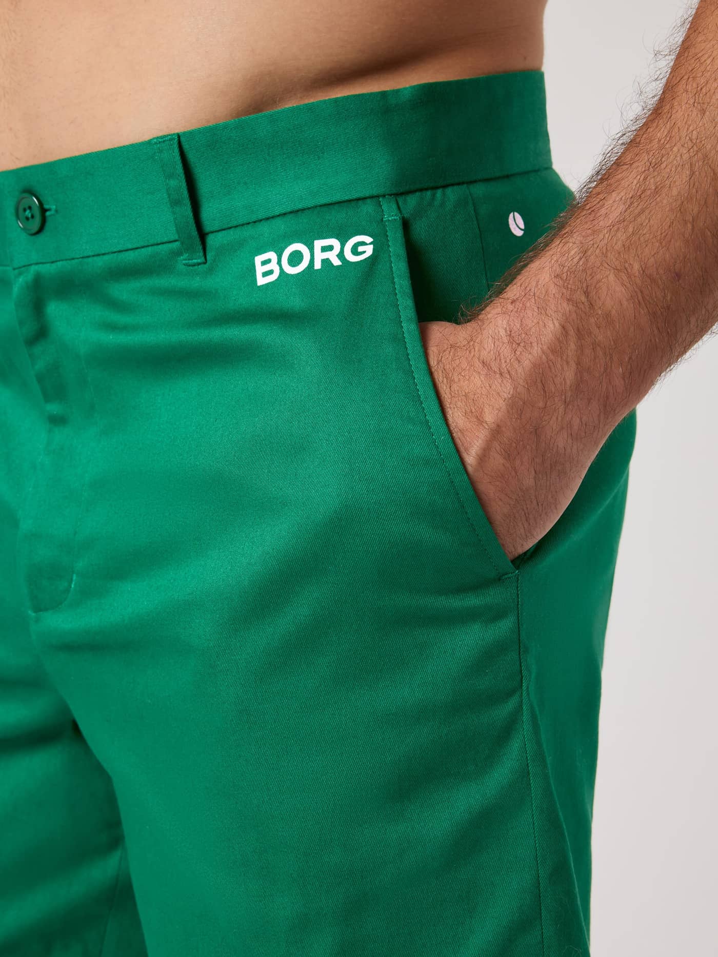 Side close-up of the Verdant Green (Green) Borg Golf Chinos Shorts featuring a white logo and tennis ball detail. - Image 4