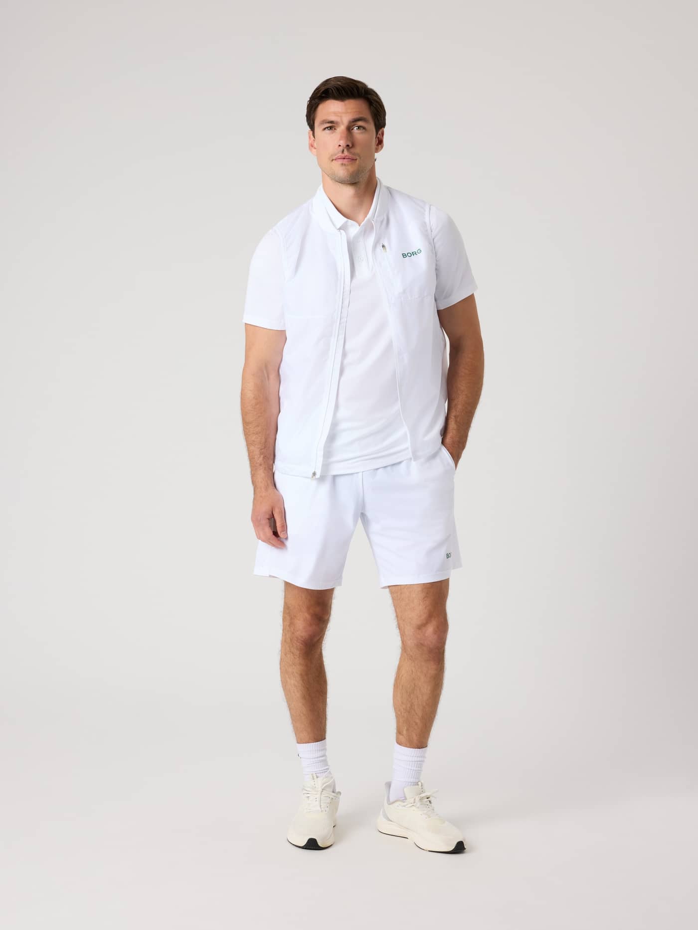 Full-body front view of a man in functional Borg Golf Sports Shorts 8 Inch in Brilliant White (White) with a green logo. - Image 3