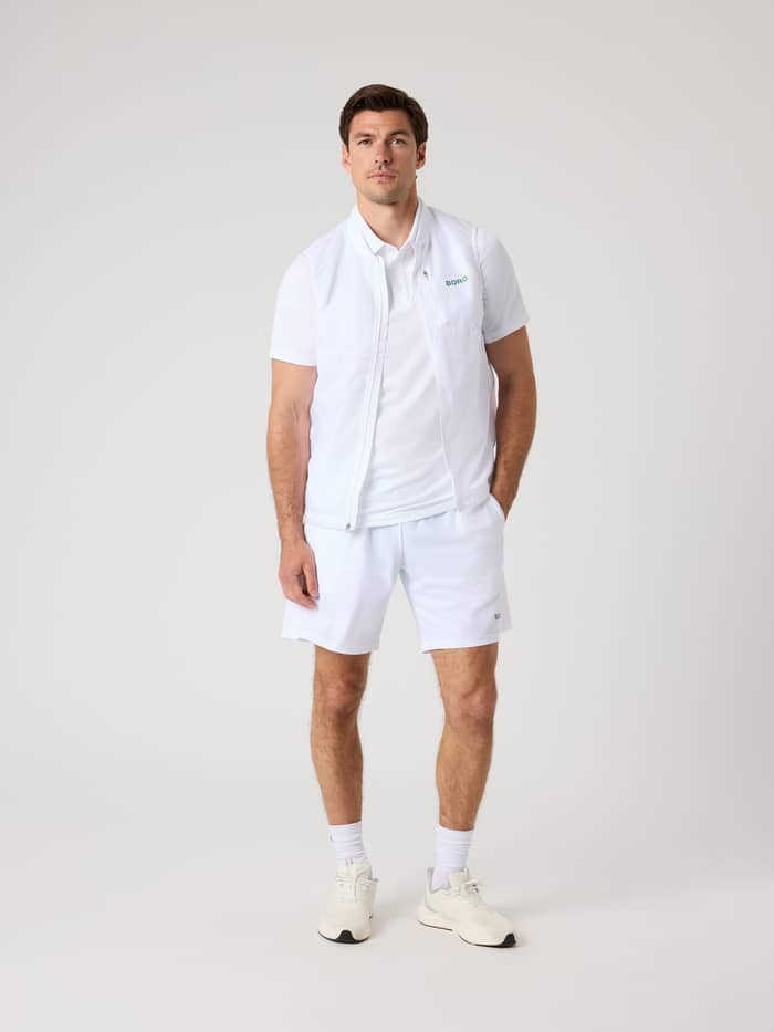 Full-body front view of a man in functional Borg Golf Sports Shorts 8 Inch in Brilliant White (White) with a green logo. - Image 3