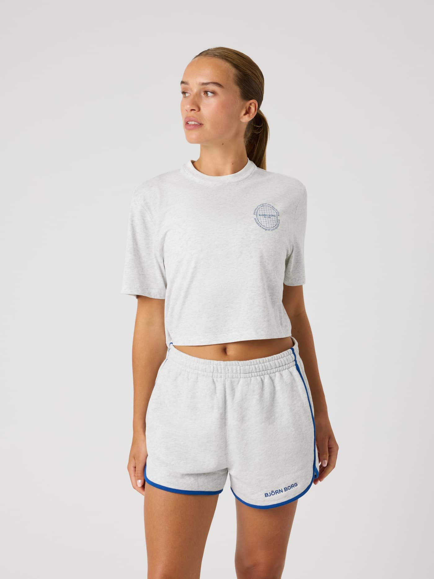 Front view of a model in the Björn Borg Studio Oversized Cropped T-Shirt in Ultra Light Grey Melange (Grey) with tennis logo. - Image 1