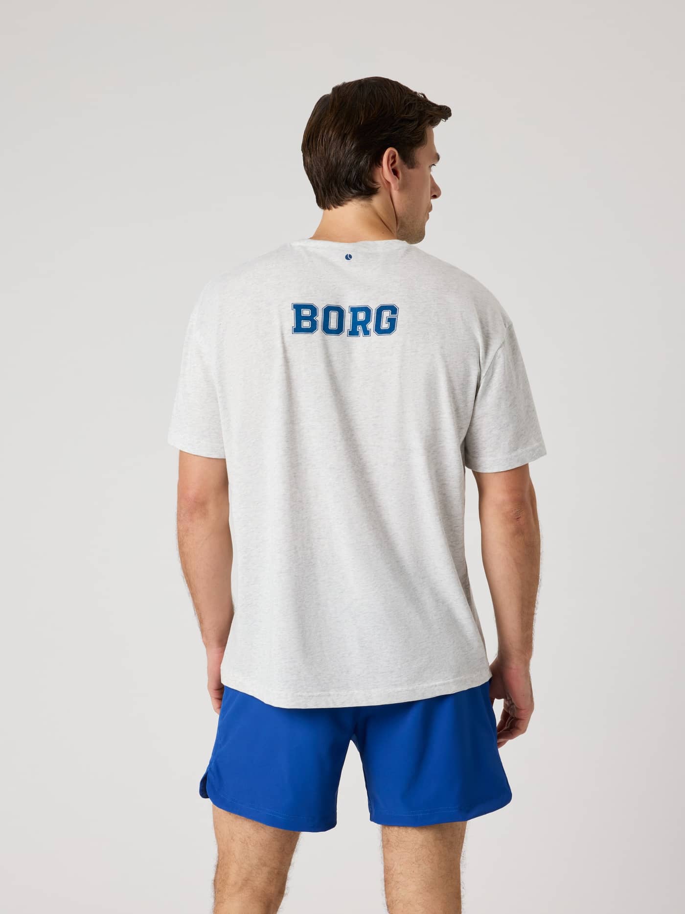 Back view of a man wearing the Ace Oversized T-Shirt in Ultra Light Grey Melange (Grey) with a blue Borg tennis print. - Image 2