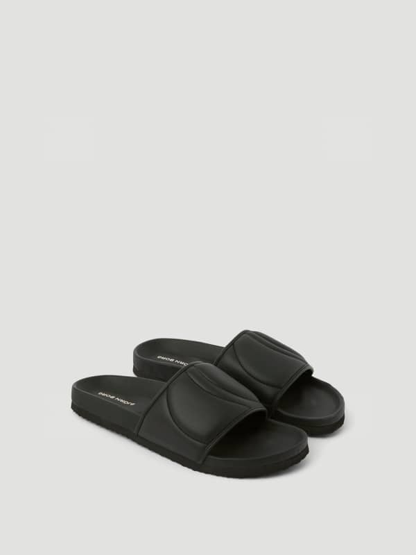 Vue en perspective des Unisex Timeout Slides noirs en TPU résistant avec logo blanc sur l'assise plantaire.