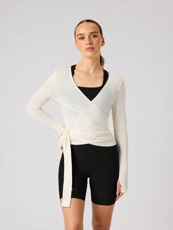 Vue de face d'un modèle portant le Studio Wrapped Top en Tofu (blanc) avec une taille cache-cœur pour le training.