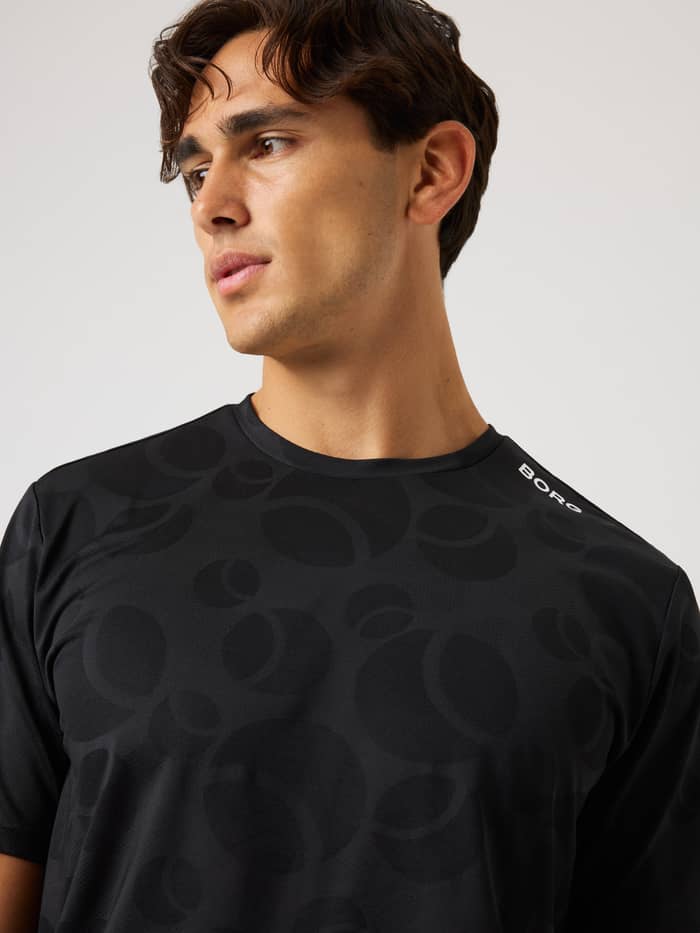 Close-up of the Ace Performance T-Shirt in Black Beauty (Black) with a tonal tennis ball pattern and white Borg logo.