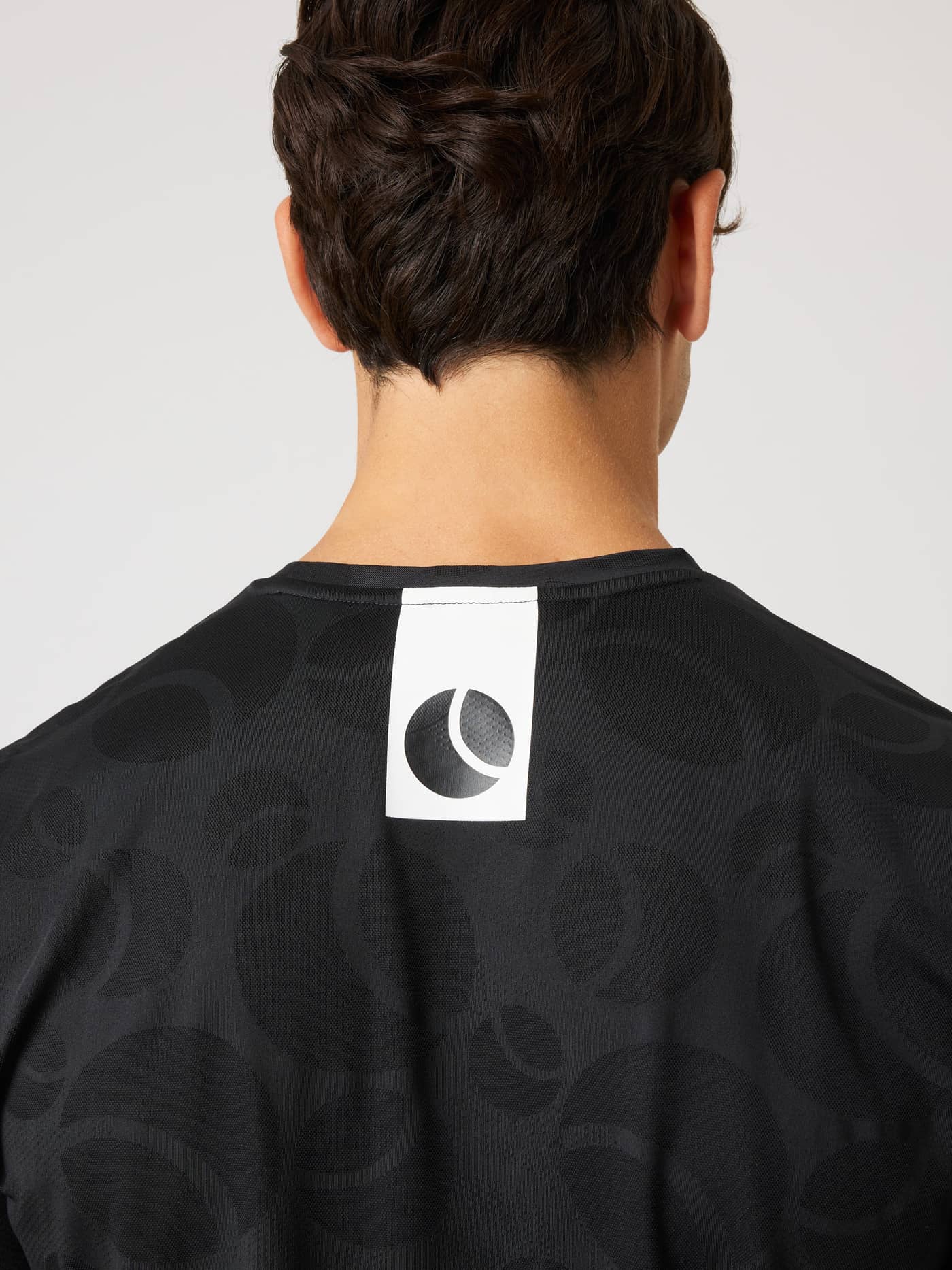 Back view of the Ace Performance T-Shirt in Black Beauty (Black) with a tennis ball jaquard pattern and white logo detail. - Image 5