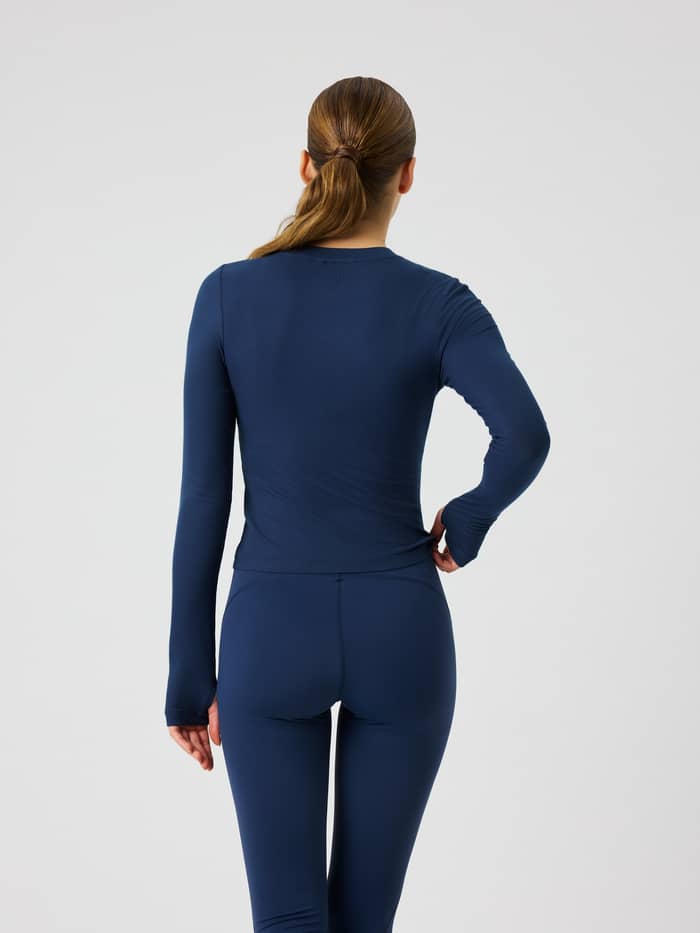 Back view of the Studio Ribbed Cropped Long Sleeve in Dress Blues (Blue) with thumbholes.