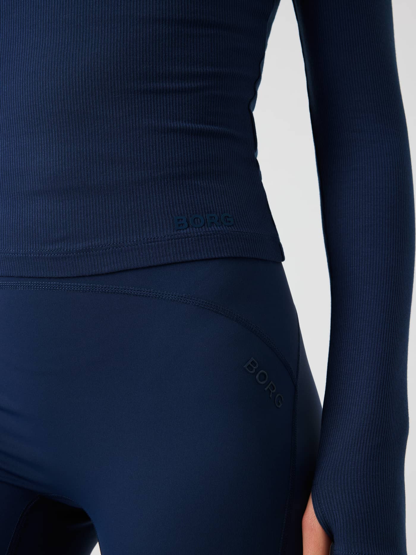 Närbild på Studio Ribbed Cropped Long Sleeve i Dress Blues (blå) med fokus på Borg-logotypen nedtill fram. - Image 6
