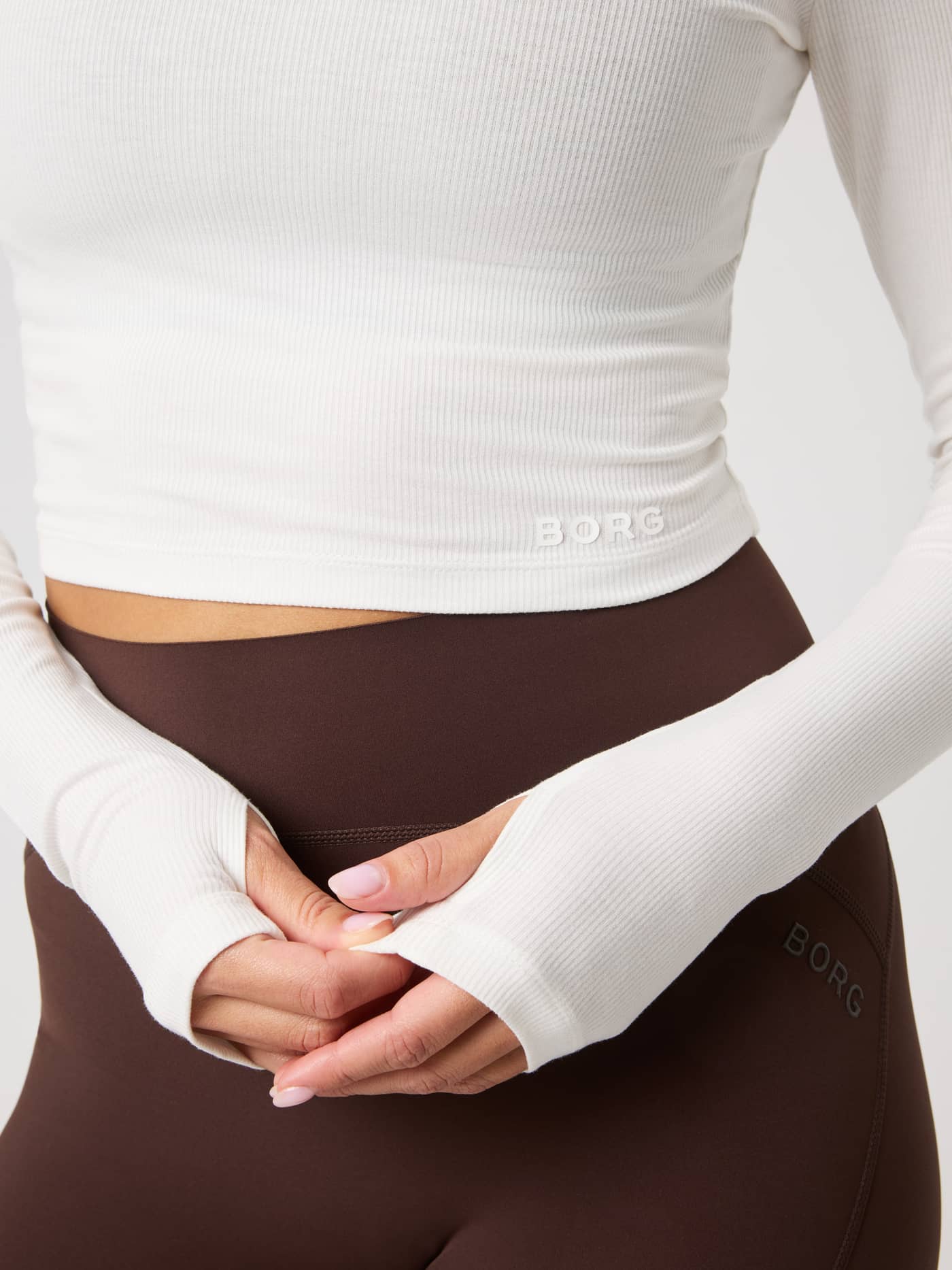 Close-up of the Studio Ribbed Cropped Long Sleeve in Tofu (White) featuring thumb holes and white Borg logo for training. - Image 6