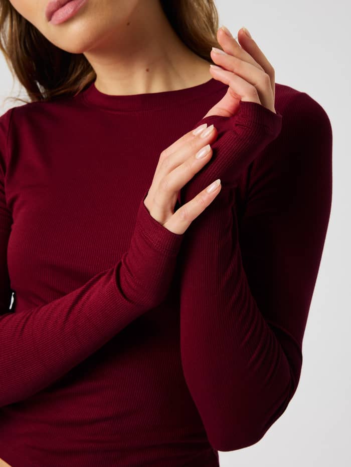 Close-up of the Studio Ribbed Cropped Long Sleeve in Cabernet (Red) highlighting the ribbed fabric and thumbhole sleeves.