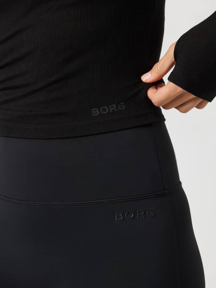 Detail van de Studio Ribbed Cropped Long Sleeve in Black Beauty (Zwart), met nadruk op de Borg-print onderaan de voorkant.