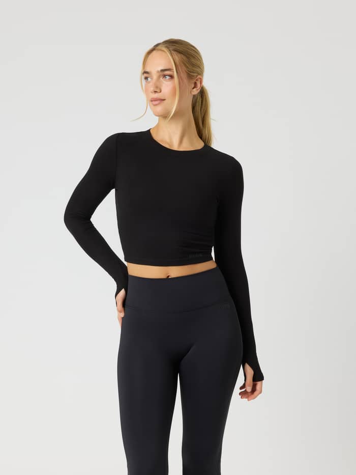 Front view of the Studio Ribbed Cropped Long Sleeve in Black Beauty (Black) with thumb holes and a black logo for training.