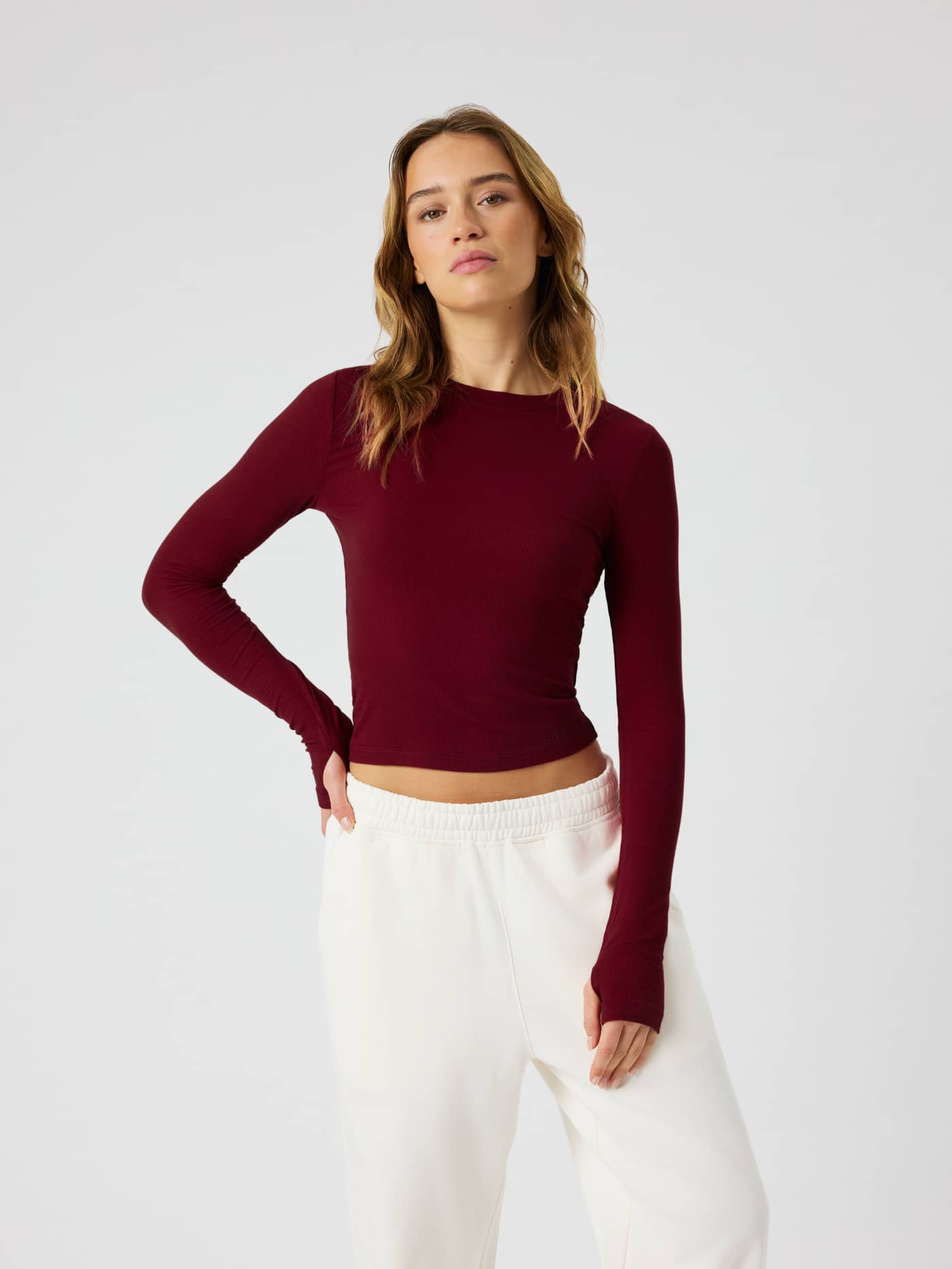 Studio Ribbed Cropped Long Sleeve i Cabernet (Rött) på en kvinna sedd framifrån med rund hals och tumhål i ärmarna. - Image 1